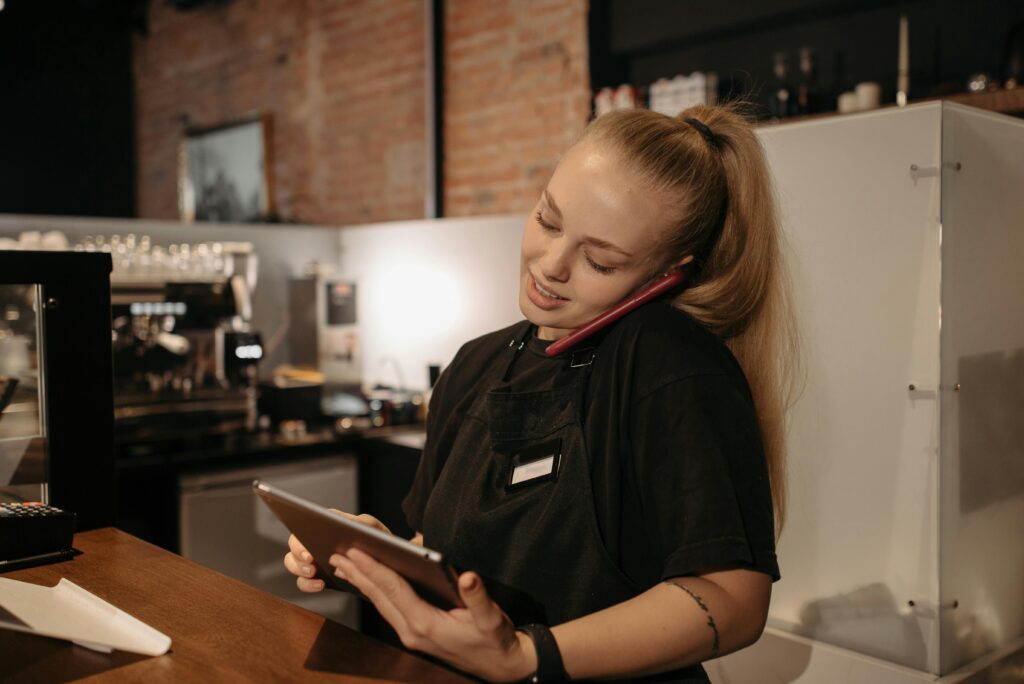 The "Hidden" SEO: Why Performance Beats "Pretty" (And Why Your Website Shouldn't Break the Bank) Young woman in café multitasks with a tablet and phone at the counter.